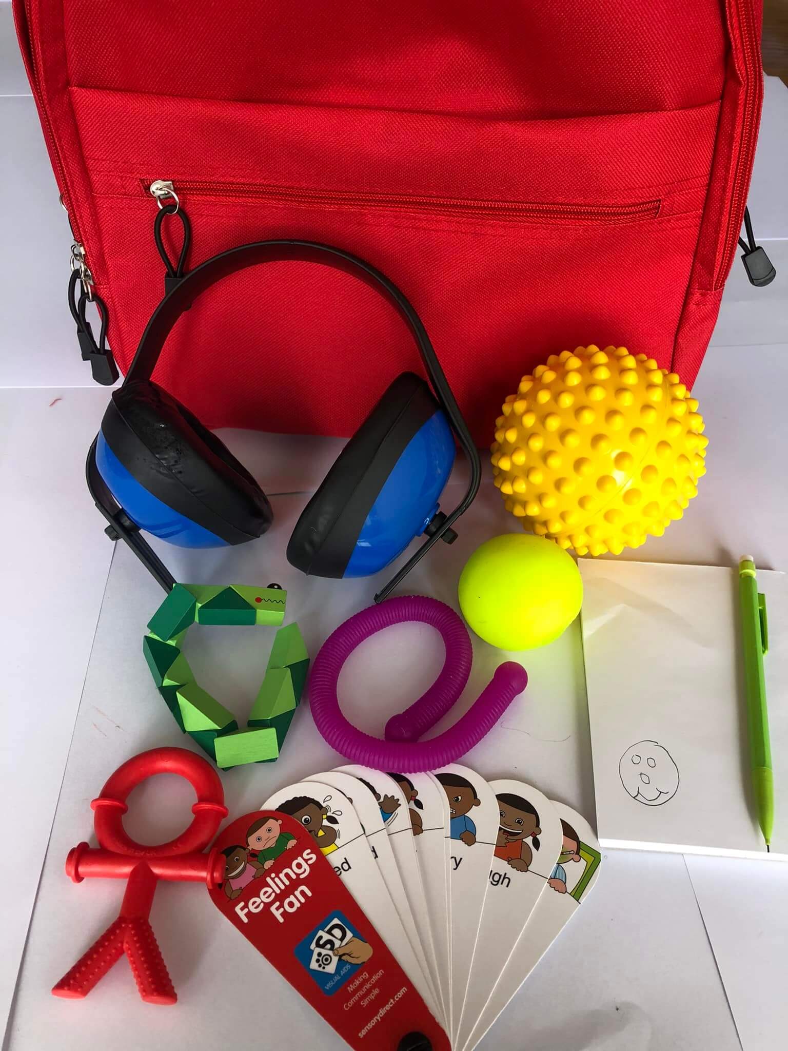 A red backpack with various sensory toys, including ear defenders, fidget toys, a notepad and pencil and emotion cards