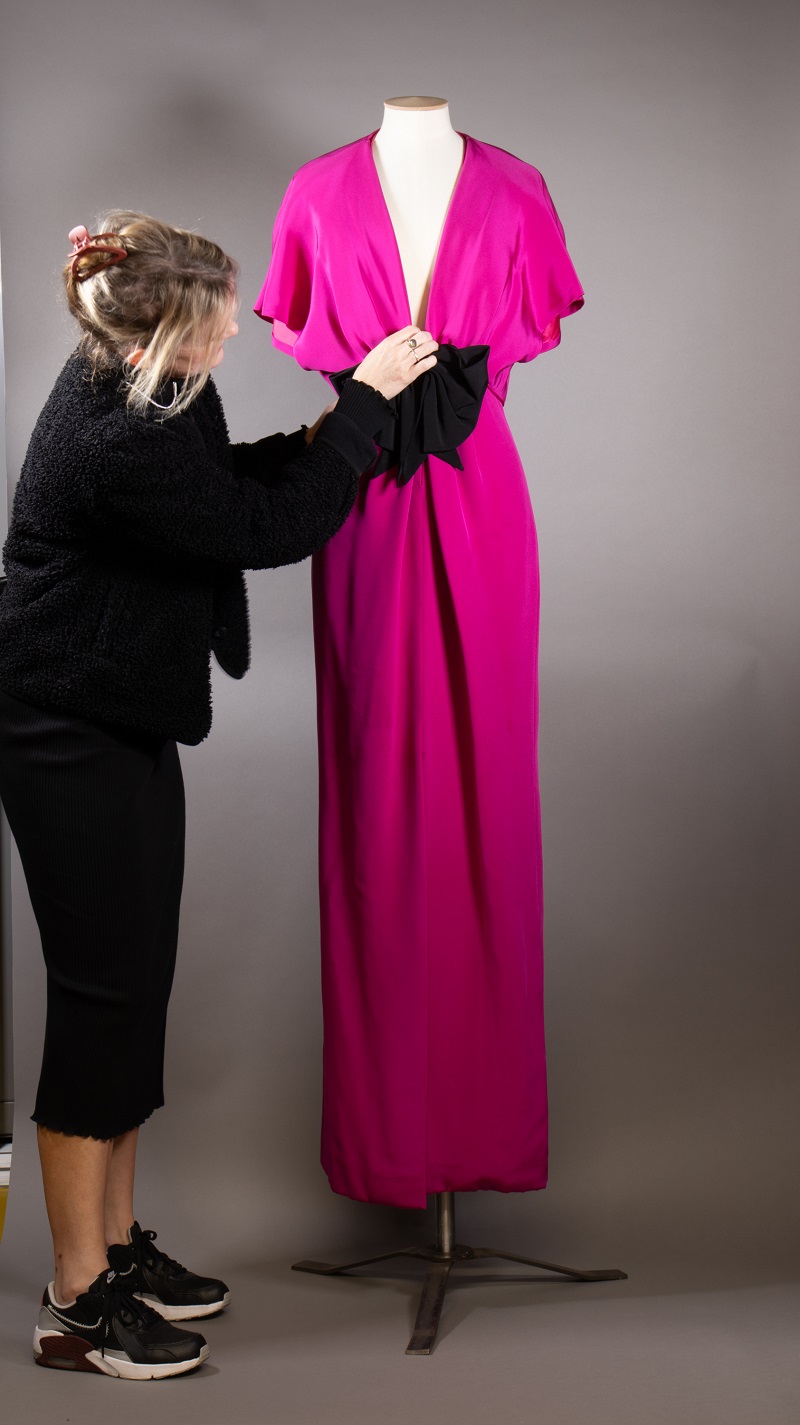 Curator Vicky arranges a pink evening dress on a mannequin