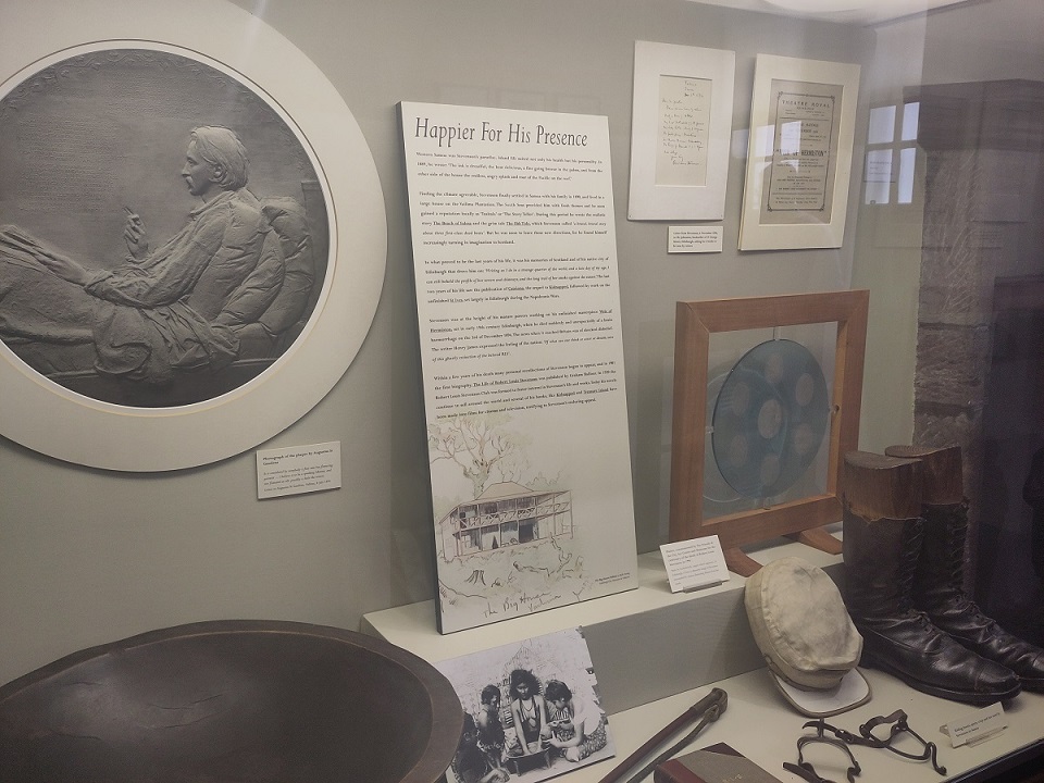 Objects on display in a museum case, including boots worn by Robert Louise Stevenson