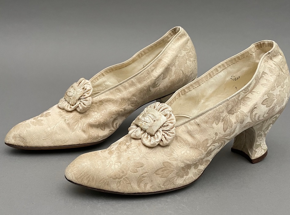 Pair of cream silk wedding shoes against a grey backdrop