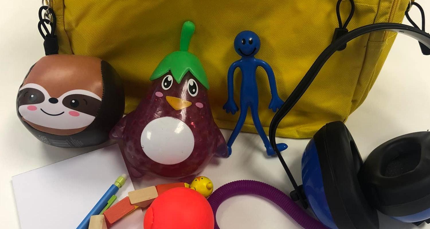 A yellow backpack with various sensory toys, including ear defenders, fidget toys, a notepad and pencil and emotion cards