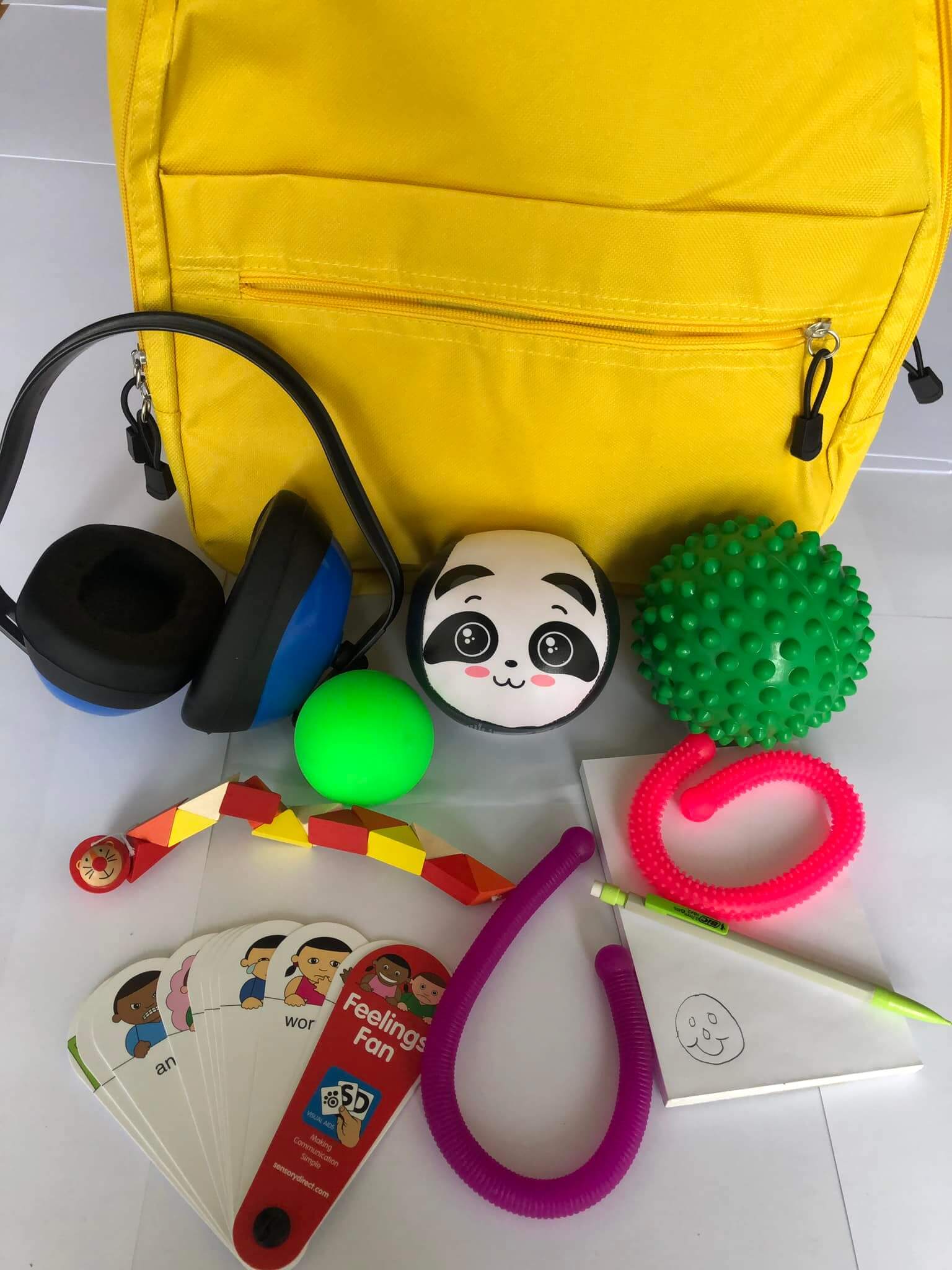 A yellow backpack with various sensory toys, including ear defenders, fidget toys, a notepad and pencil and emotion cards