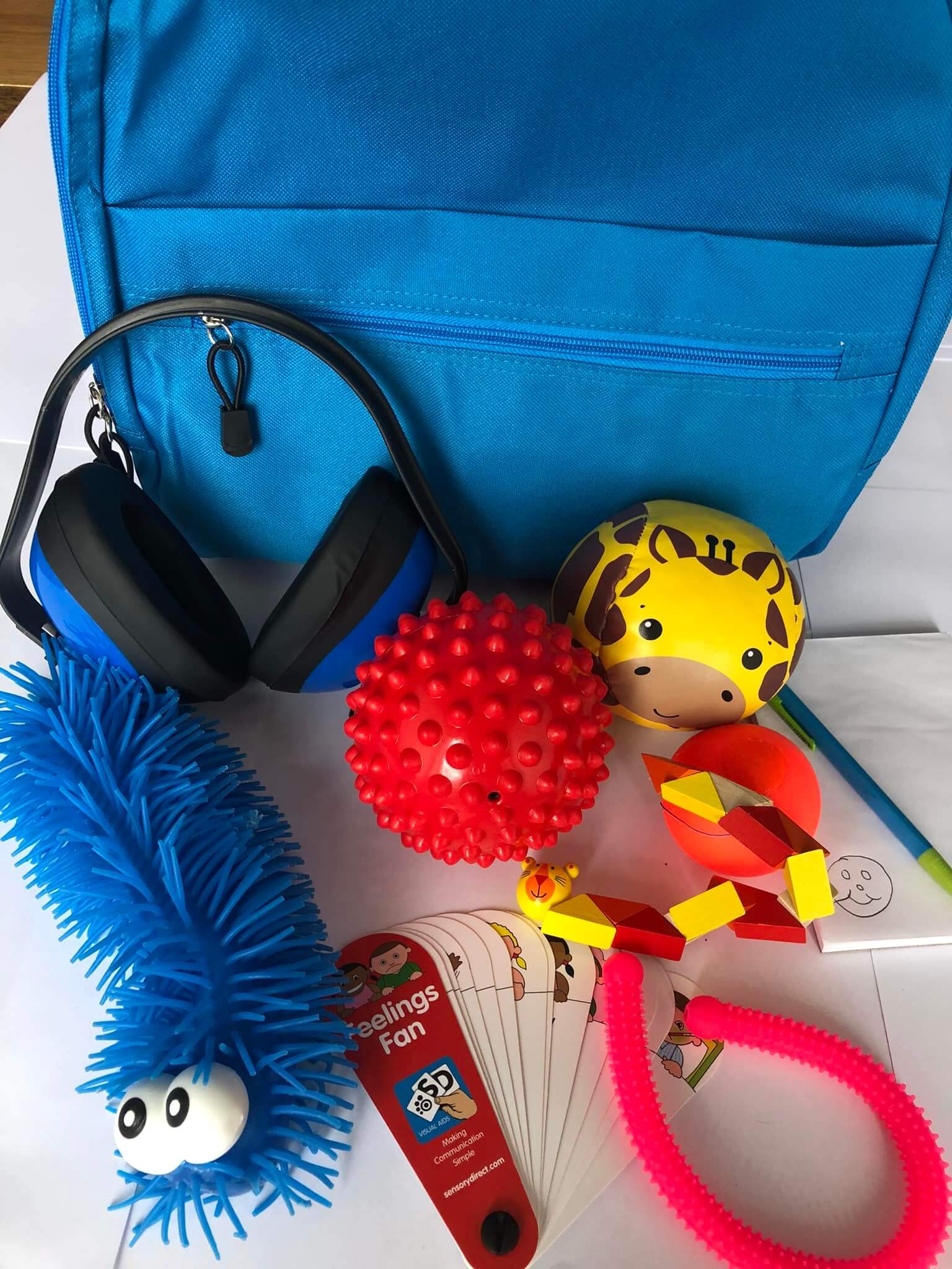 A blue backpack with various sensory toys, including ear defenders, fidget toys, a notepad and pencil and emotion cards