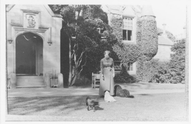 A black and white photo of a woman in a long dress outside the entrance to the Castle with three dogs