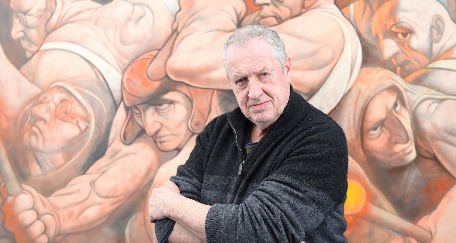Photo of artist Peter Howson in front of one of his paintings