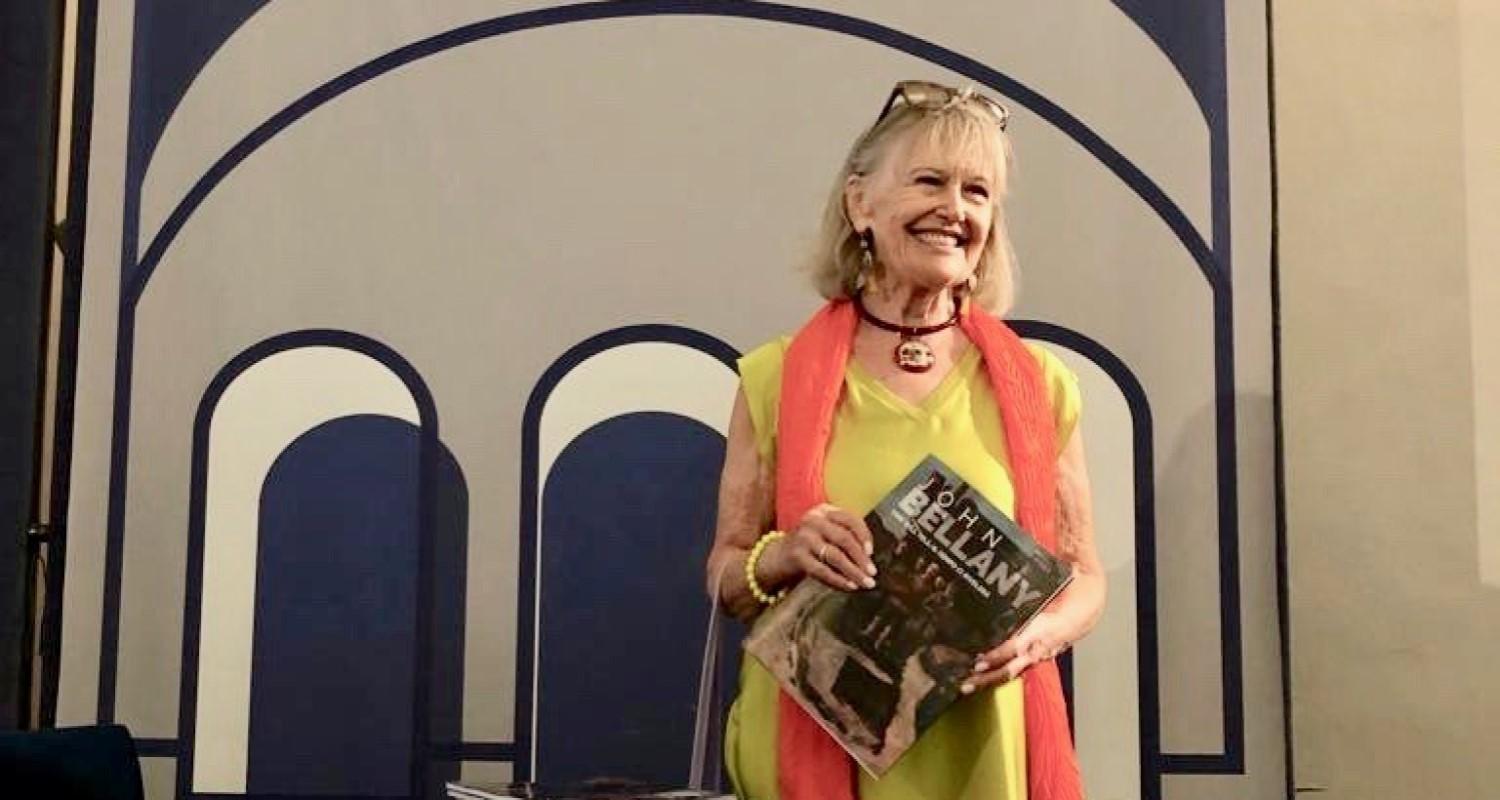 Helen Bellany in a lime dress and orange scarf holding a book entitled John Bellany