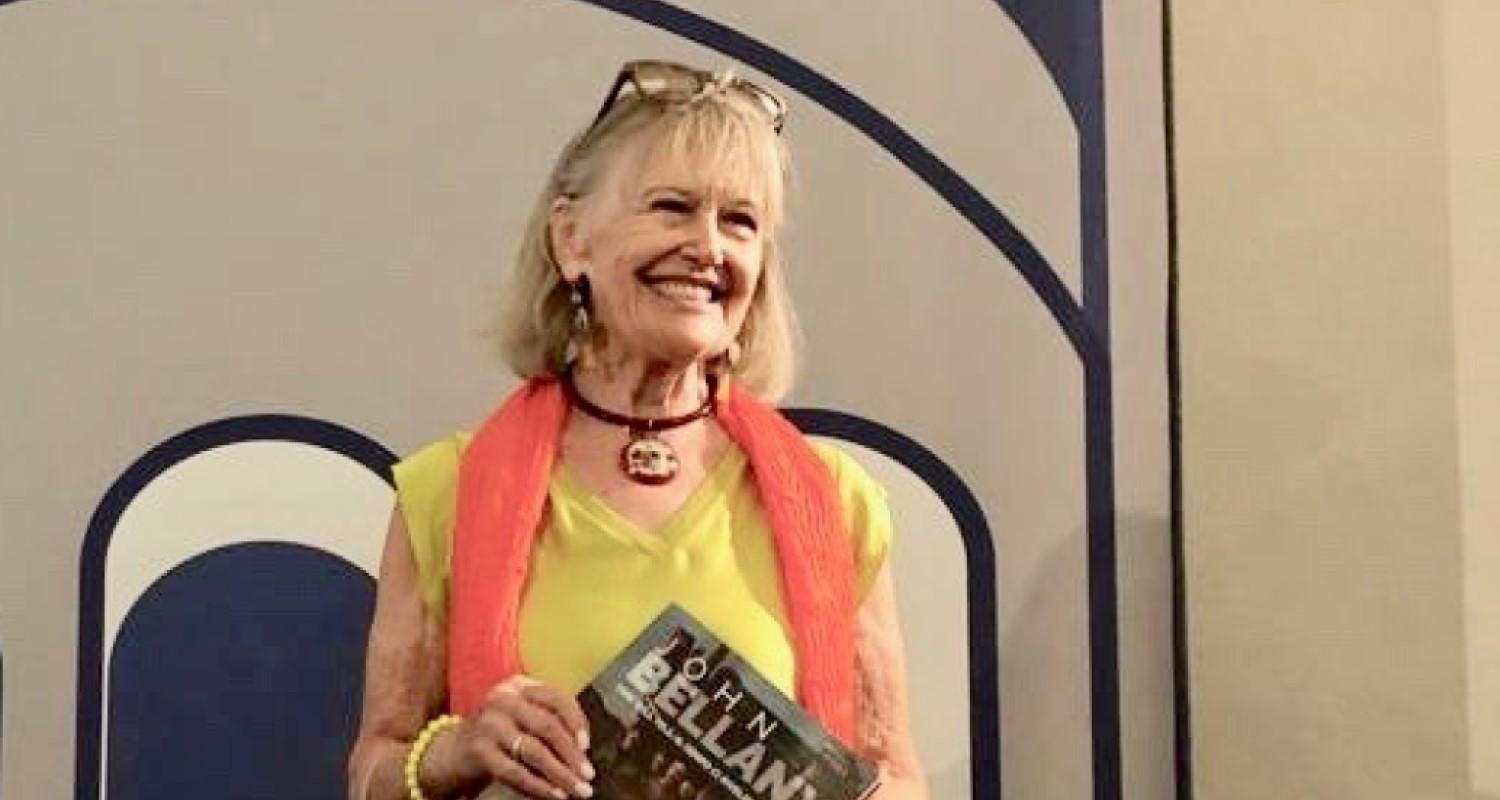 Helen Bellany in a lime dress and orange scarf holding a book entitled John Bellany