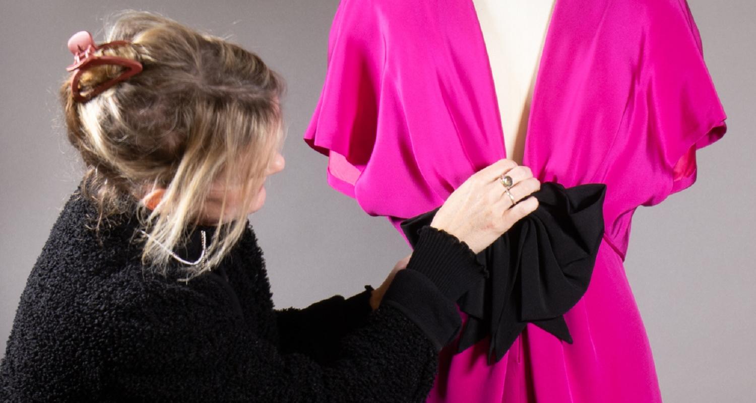 Curator Vicky arranges a pink evening dress on a mannequin