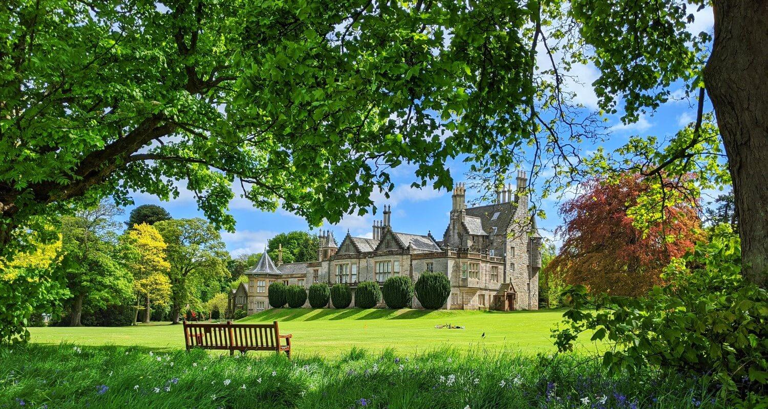 A shot of Lauriston through the trees and across the lawn. The bench is in the foreground