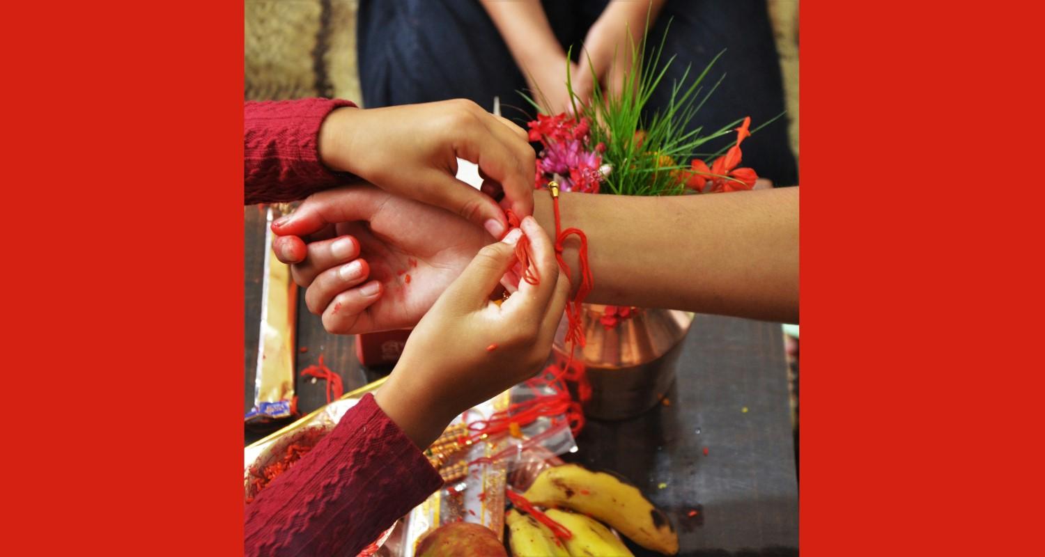 Hands tying a rakhi - red string - bracelet onto a wrist