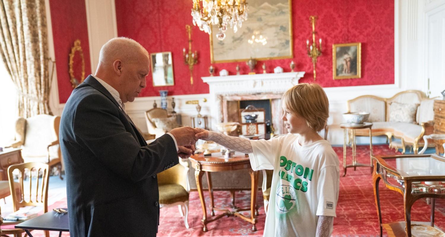 A magician in a suit shakes hands with a young boy in the drawing room at Lauriston