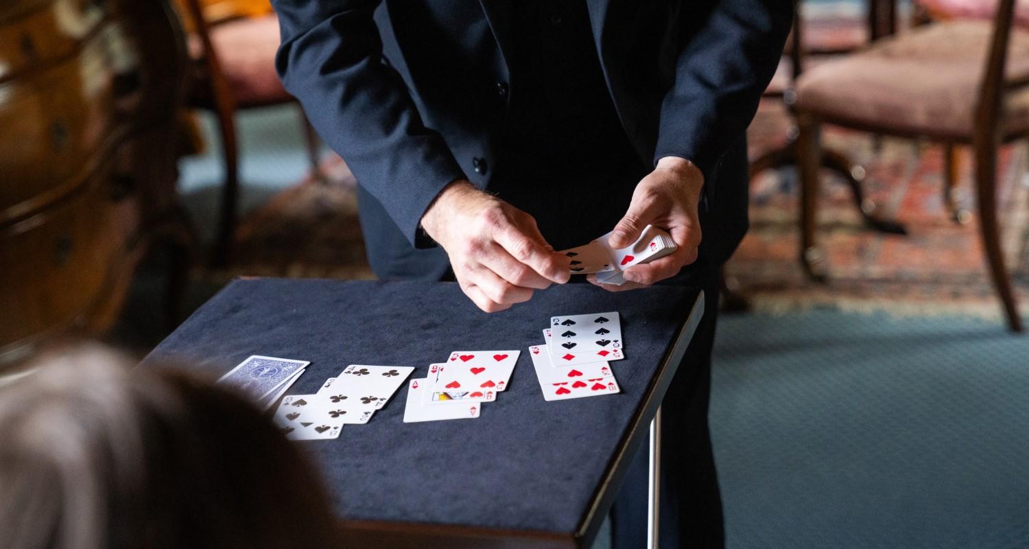 A magician deals a pack of cards onto a small grey baize table