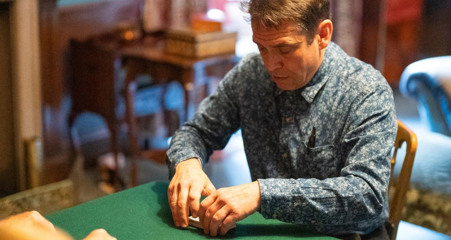 A magician cutting cards on a green baize table