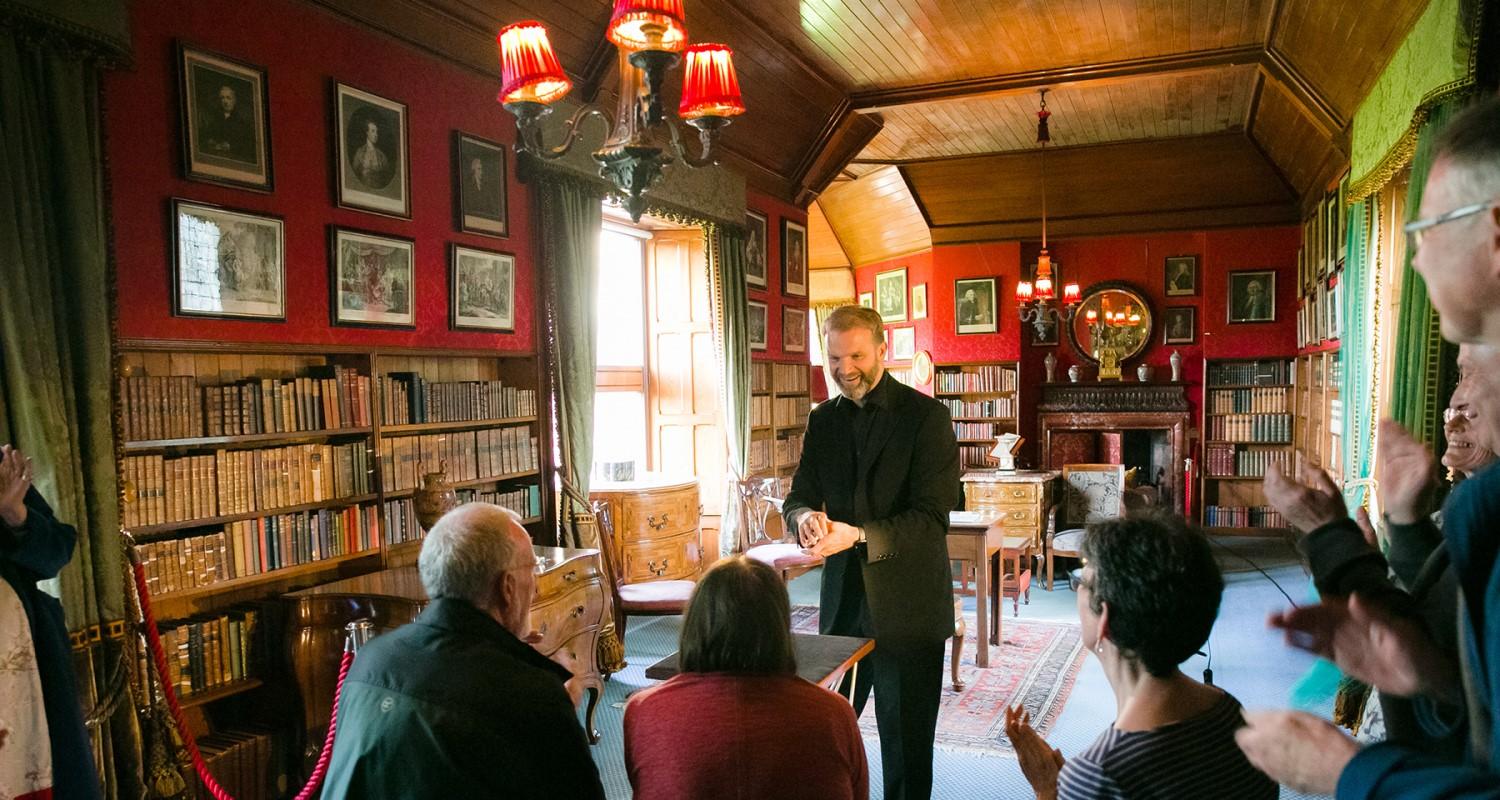 A magician and audience in the library. The audience is applauding.