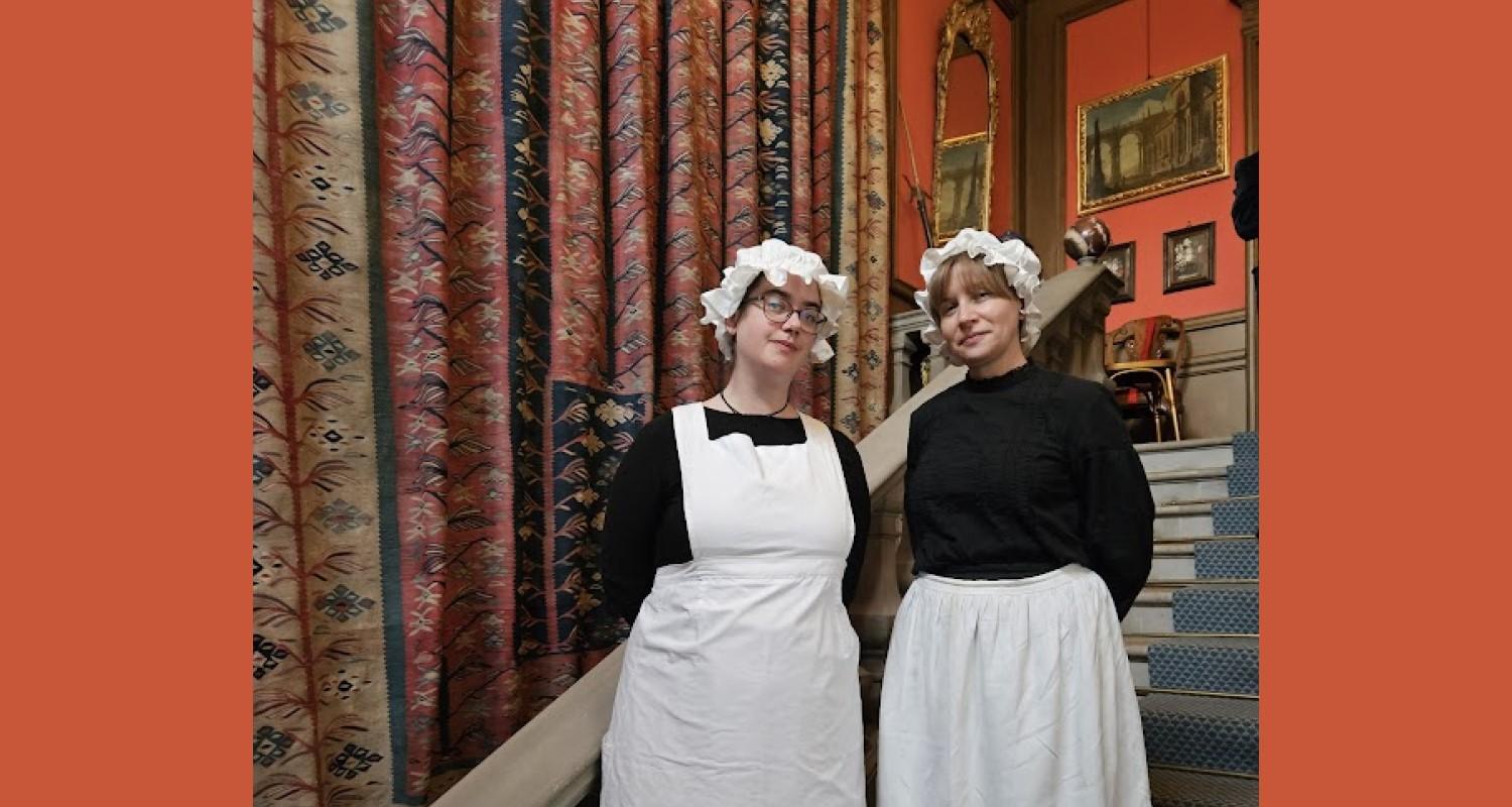 Two kitchen staff in Edwardian black and white uniforms stand on the stairs at Lauriston