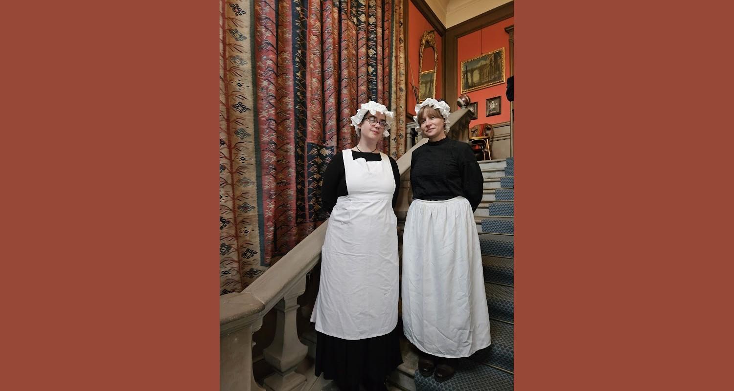 Two kitchen staff in Edwardian black and white uniforms stand on the stairs at Lauriston