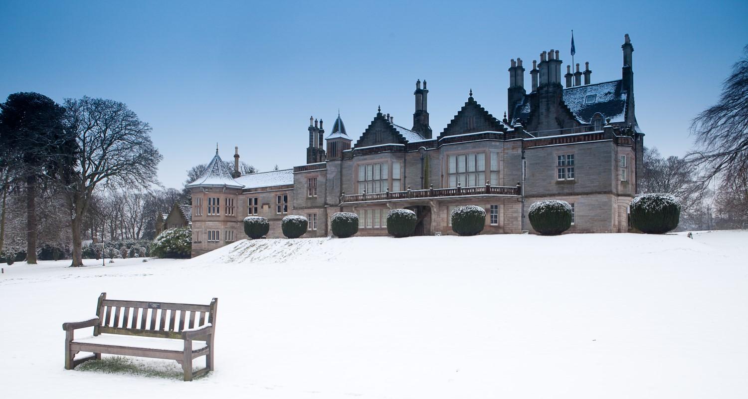 A shot of the exterior of Lauriston from the front on a snowy day. The garden bench is in the foreground and the skies are blue