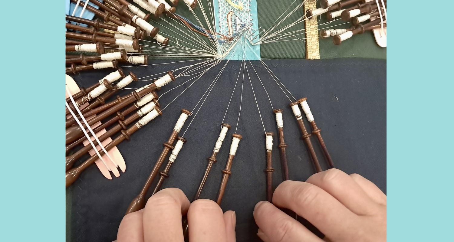 Two hands holding wooden bobbins of a lace work in progress