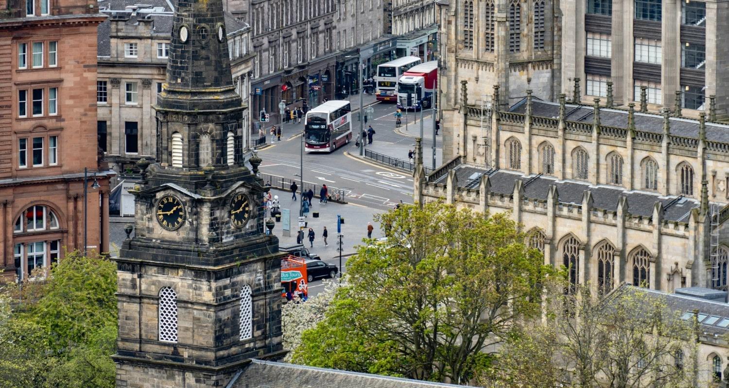 An aerial photograph showing the clock tower of St Cuthbert's church and the Caledonian Hotel in the foreground and St John's Church in the background, with traffic driving along Lothian Road and Queensferry Street