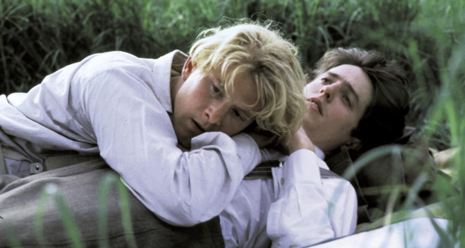 A still from the film Maurice showing James Wilby and Hugh Grant lying in a field