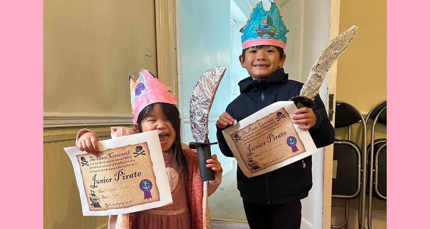 A boy and girl with pirate hats and swords proudly showing off their Junior Pirate certificates