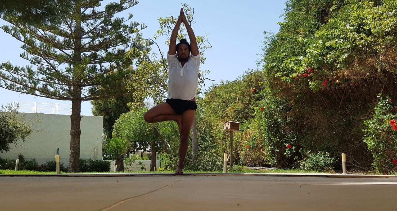 A man in a tshirt and shorts standing outside doing a yoga pose