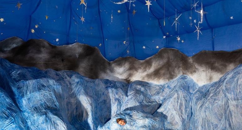 An artistic impression of a dark blue sky at night, filled with bright stars and a moon, overlooking dark hills