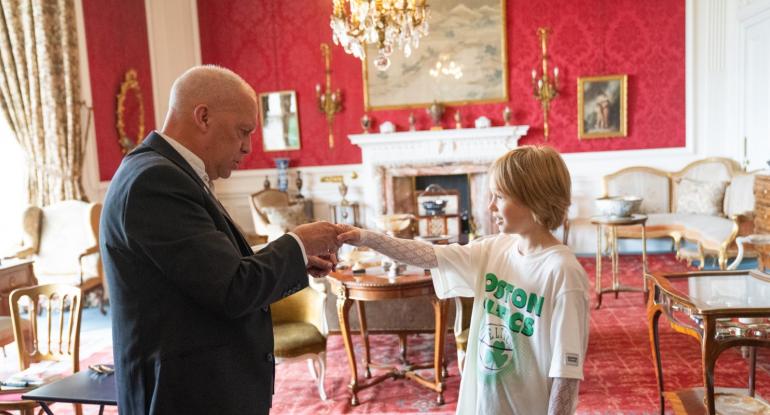 A magician in a suit shakes hands with a young boy in the drawing room at Lauriston