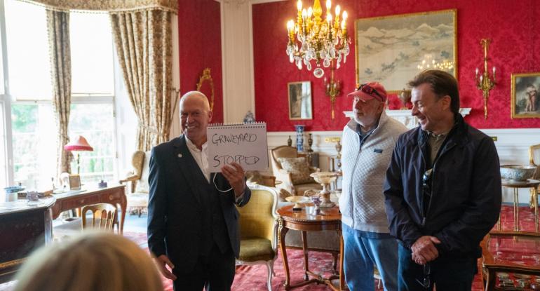 A magician holds a sign saying GRAVEYARD STOPPED as two participants from the audience look on