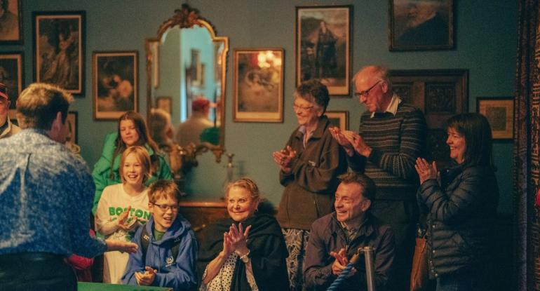 A shot of the audience applauding the magician. The wall in the background is covered in pictures