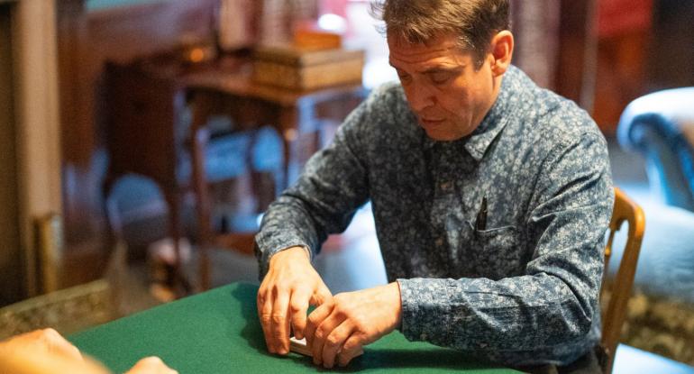 A magician cutting cards on a green baize table