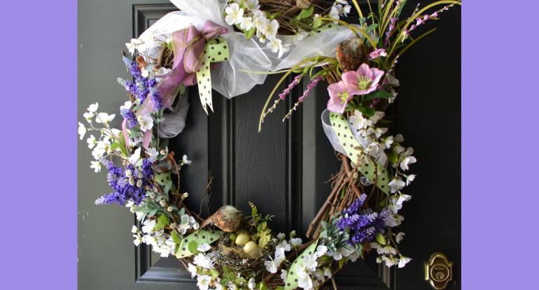 A wreath of spring flowers and ribbons with little birds nests and fake birds against a black door