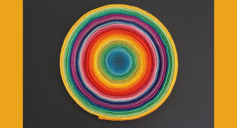 Circles of fabric on a black background shown edges up, each of a different colour, starting from yellow at the outside through green purple and pink, to red, yellow, green and blue at the centre