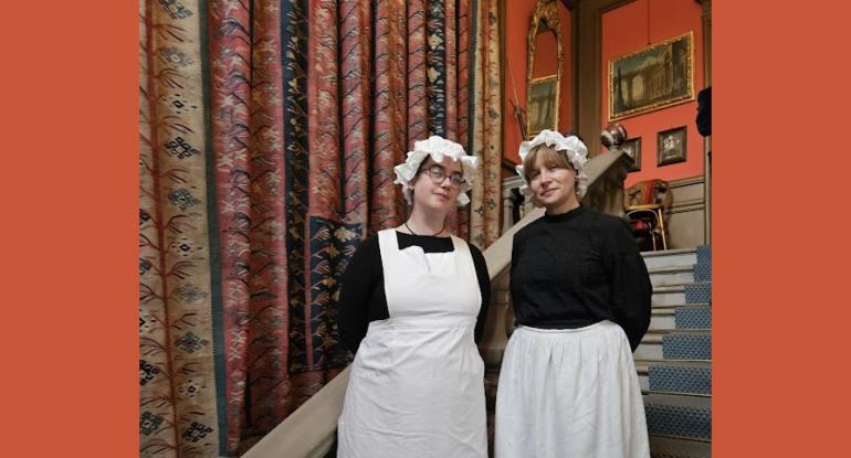 Two kitchen staff in Edwardian black and white uniforms stand on the stairs at Lauriston