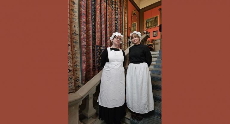 Two kitchen staff in Edwardian black and white uniforms stand on the stairs at Lauriston