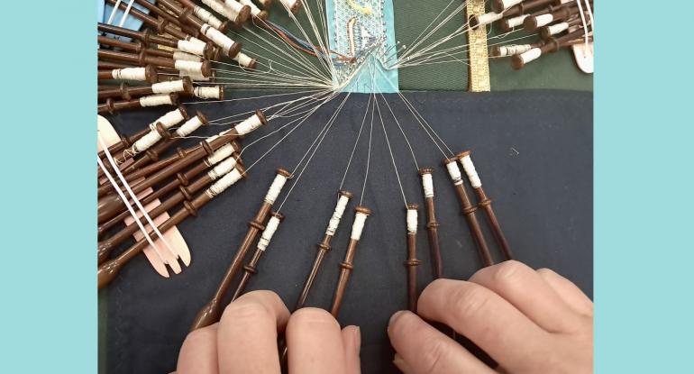 Two hands holding wooden bobbins of a lace work in progress