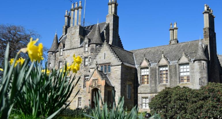 Lauriston Castle underneath a blue sky. Yellow daffodils feature in the foreground