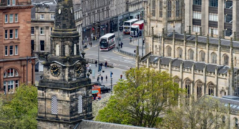 An aerial photograph showing the clock tower of St Cuthbert's church and the Caledonian Hotel in the foreground and St John's Church in the background, with traffic driving along Lothian Road and Queensferry Street