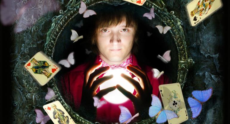 A man holding a glowing globe reflected in a circular gothic mirror with butterflies and playing cards scattered around the edges