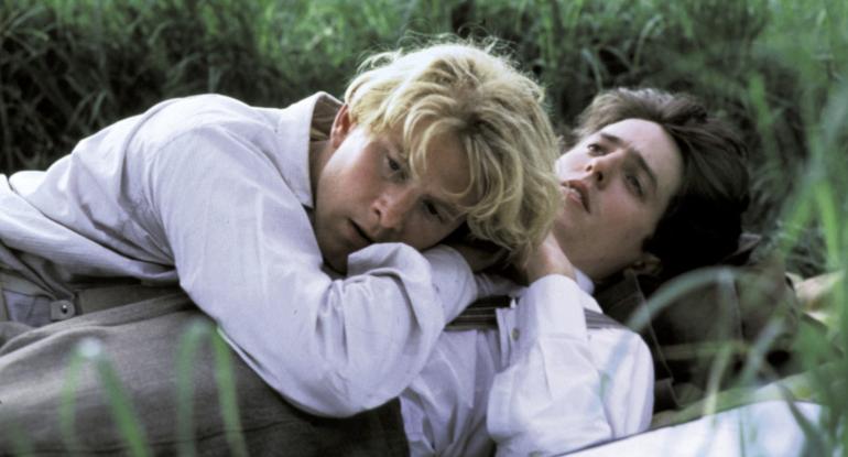 A still from the film Maurice showing James Wilby and Hugh Grant lying in a field