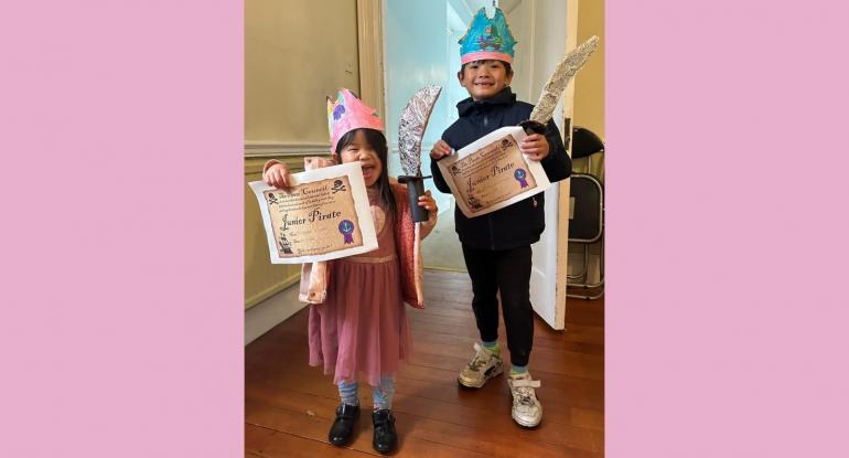 A boy and girl with pirate hats and swords proudly showing off their Junior Pirate certificates