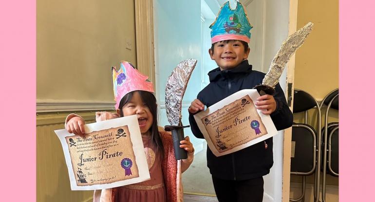 A boy and girl with pirate hats and swords proudly showing off their Junior Pirate certificates