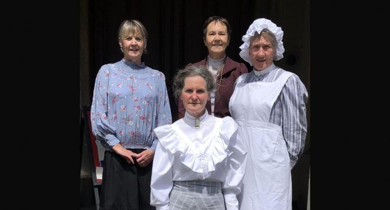 Four women, in the clothing of Edwardian staff and the Lauriston Castle owner, stand at the building's entrance