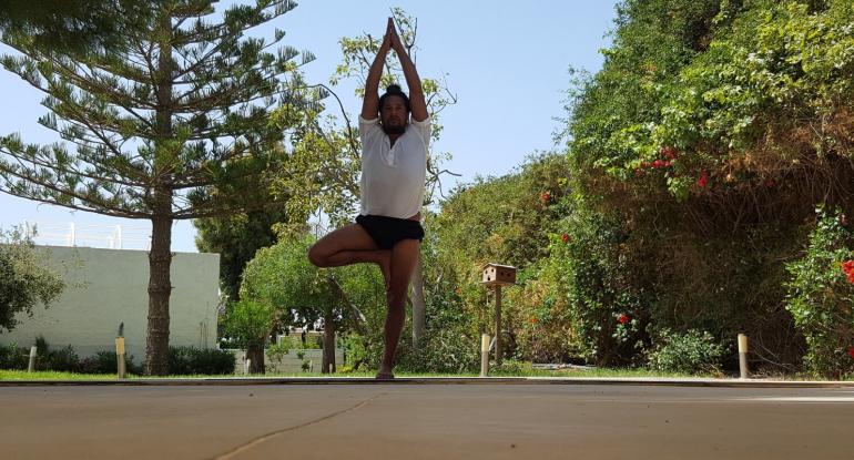 A man in a tshirt and shorts standing outside doing a yoga pose