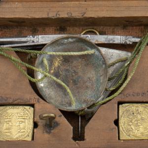 Close up of a wooden box with embossed brass square coin weights and a small weighing scale with metal pans