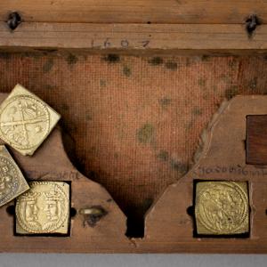 Close up of a wooden box with embossed brass square coin weights and a small weighing scale with metal pans