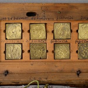 Close up of a wooden box with embossed brass square coins weights inside the lid with handwritten labels