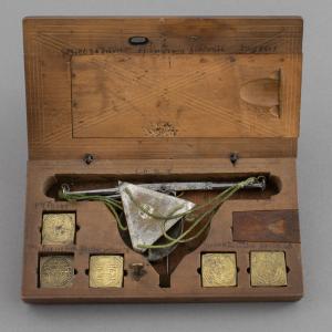 Close up of a wooden box with embossed brass square coin weights and a small weighing scale with metal pans