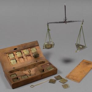 Wooden box with brass coin weights and a coin balance, seen hanging in place