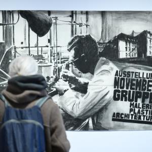 A visitor to the City Art Centre gazes thoughtfully at artwork depicting another man at work in perhaps a scientific or research role.